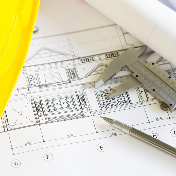 Construction plans with yellow helmet and drawing tools on blueprints